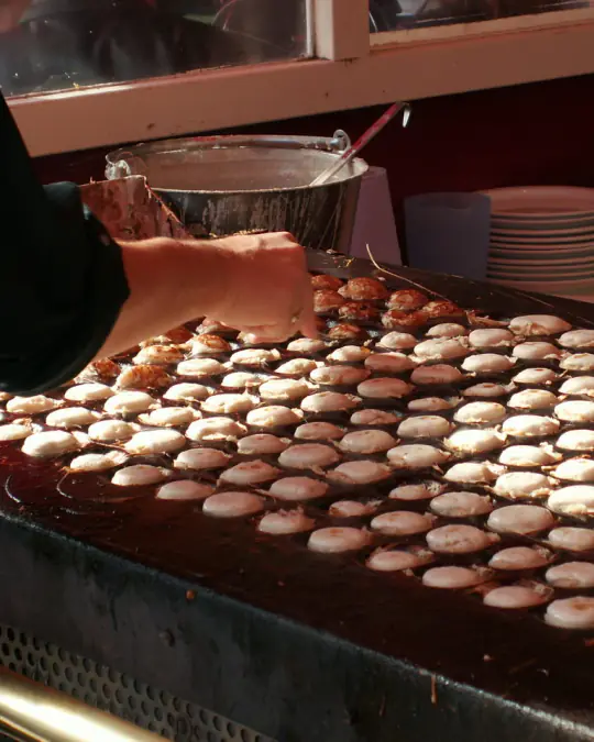 Poffertjes cooking in rows on a cast iron griddle