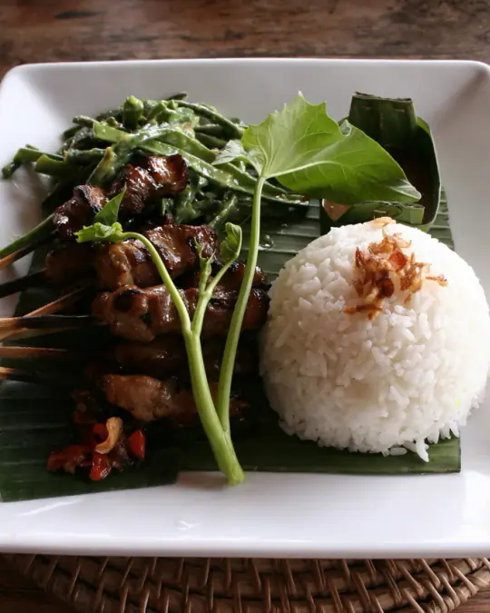 An Indonesian dish of satay skewers with rice on a banana leaf